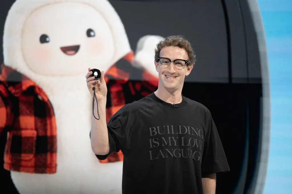 Mark Zuckerberg holding up the Muse Charm keychain device at Meta Connect 2026, with the Muse mascot on screen behind him
